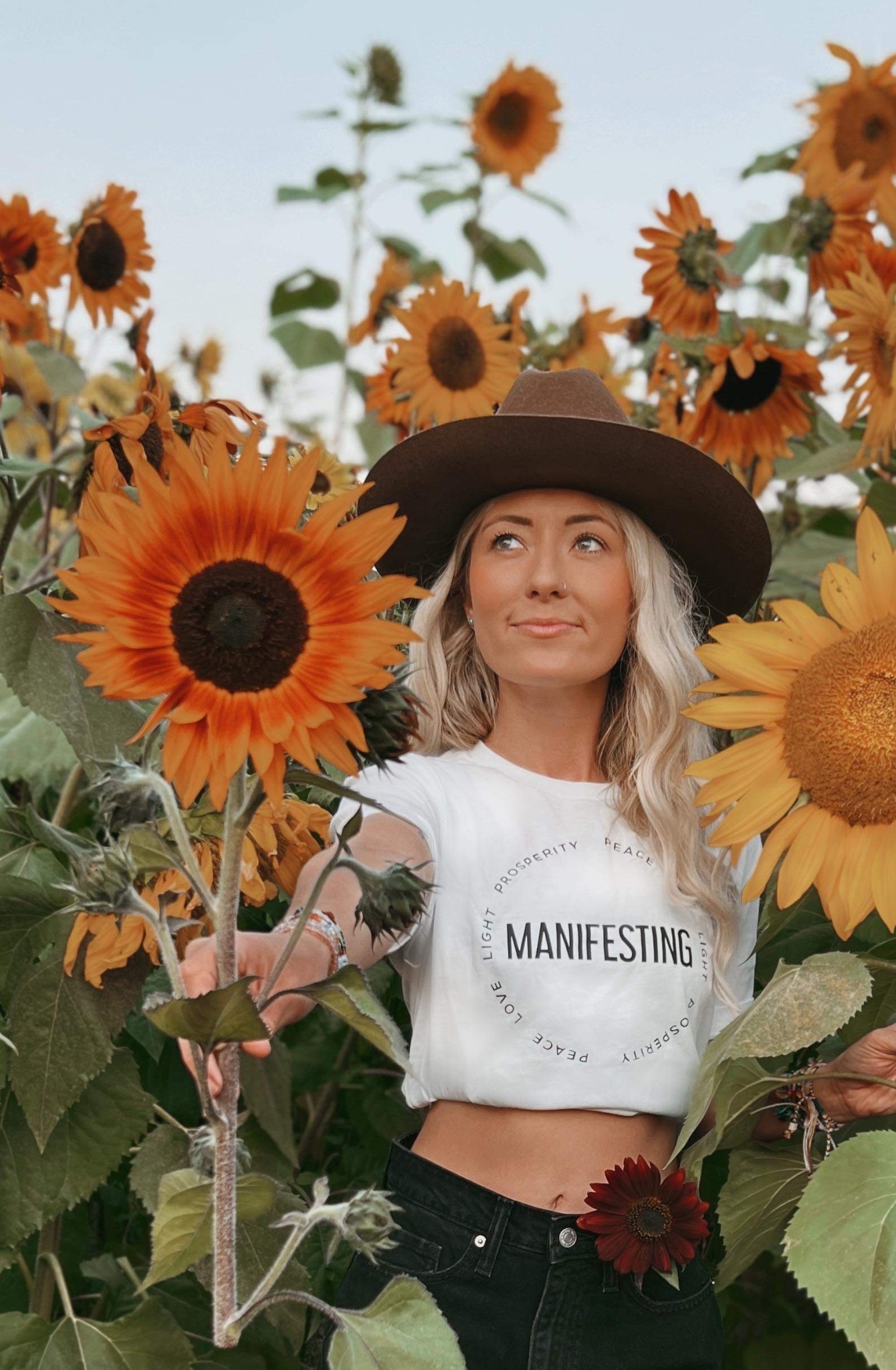 Woman holding a sunflower in a white Manifesting crop tee